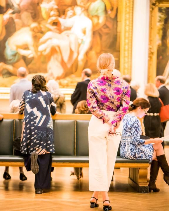 Four women in the foreground looking at three large paintings in the background