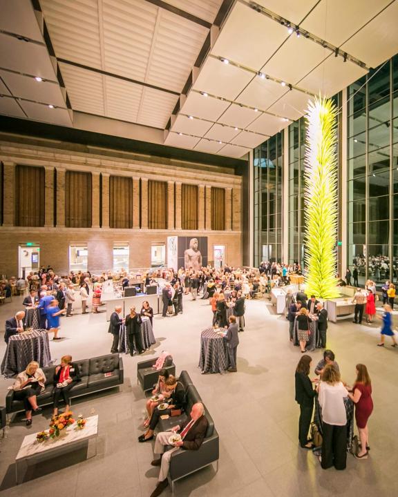 party in large indoor courtyard with large green sculpture in the background
