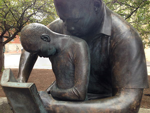 A bronze sculpture of a father reading a book with his son on his lap.