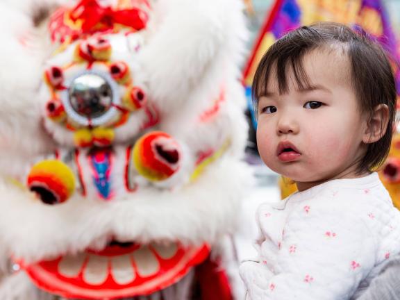 A young child stands in front of a Chinese dragon costume.