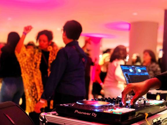 People dance in a dimly lit room while a DJ spins records.
