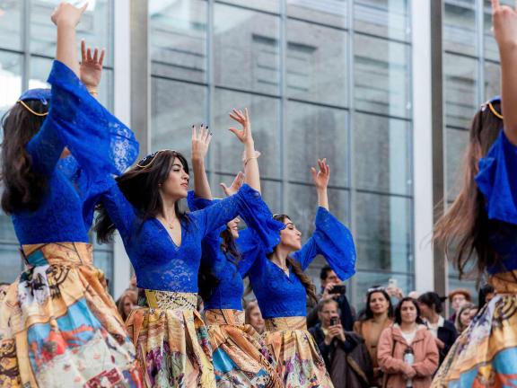 Women in blue dresses raise their arms in dance.