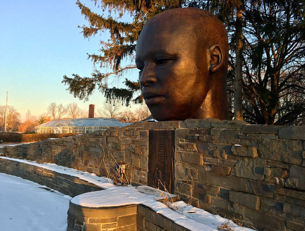 A bust of Martin Luther King Jr. sits on top of a stone wall in a snowy field at dusk.