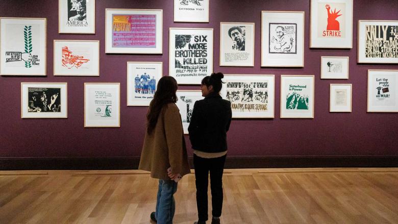 Two visitors looking at gallery wall filled with framed prints from "Power of the People" exhibition