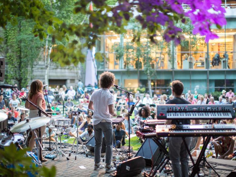 A group of musicians playing music for an audience in an open-air courtyard at dusk.