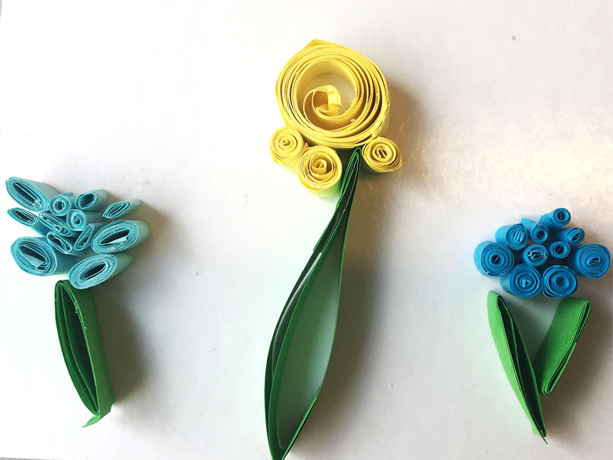 three flowers formed by quilled paper strips of various colors