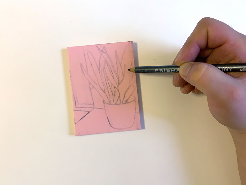 hand holding pencil to sketch image onto linoleum block
