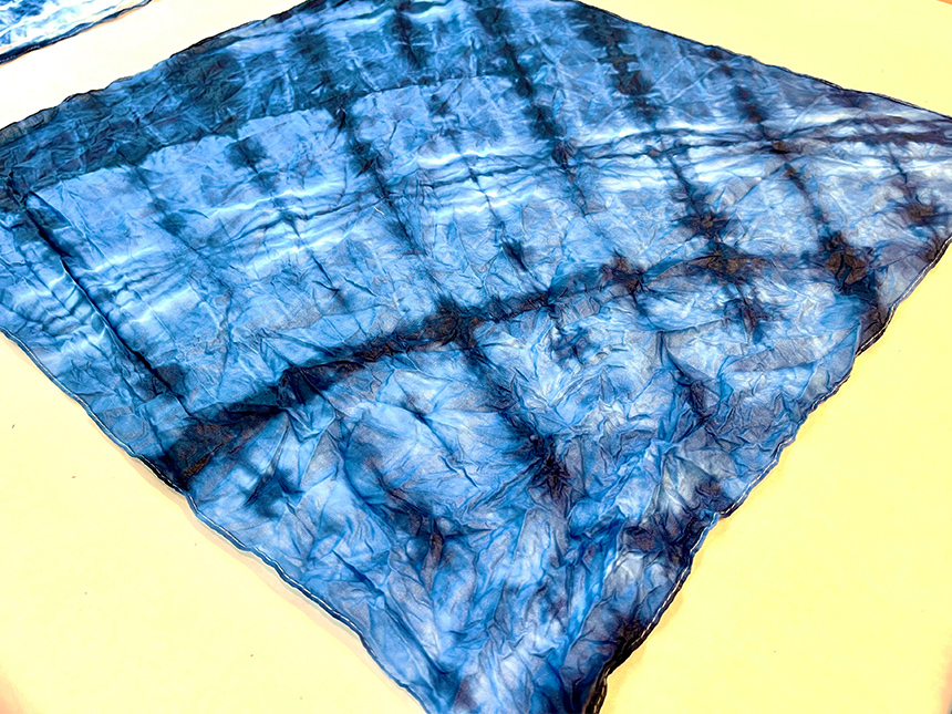 dyed fabric with shibori pattern spread open on tabletop to dry