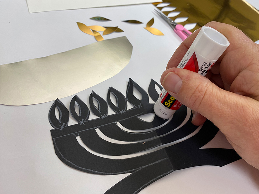 using gluestick to apply glue to the back of the black cut-out Hanukkiah