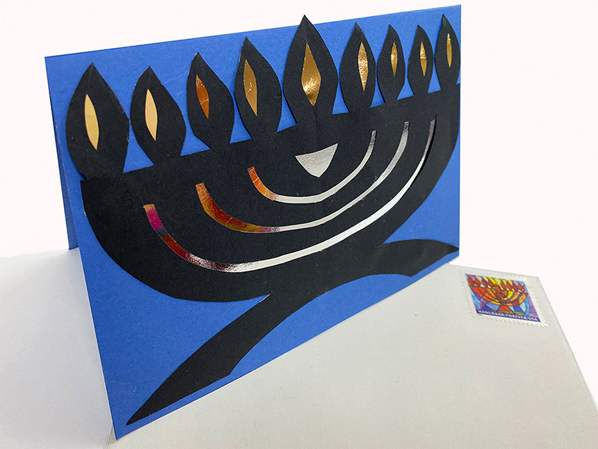 paper cut-out of Hanukkiah on blue card, propped on top of white envelope with Hanukkah stamp