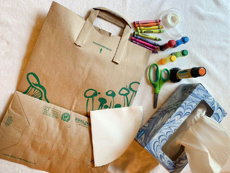 craft materials laid out, including paper grocery bag, crayons, tape, scissors, and a box of tissues