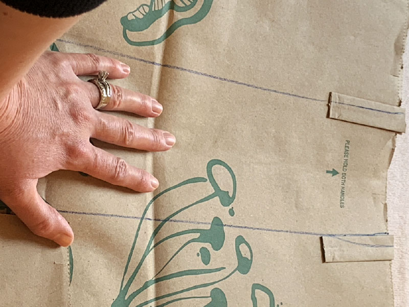 hand holding down paper bag while two vertical lines are drawn on bag