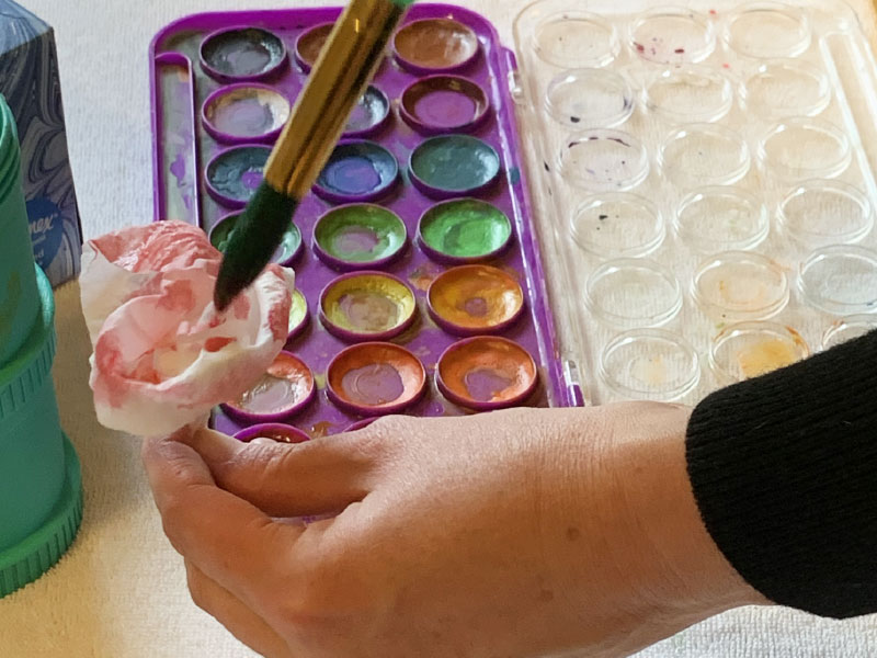 using paintbrush to dab watercolor paint onto tissue flowers