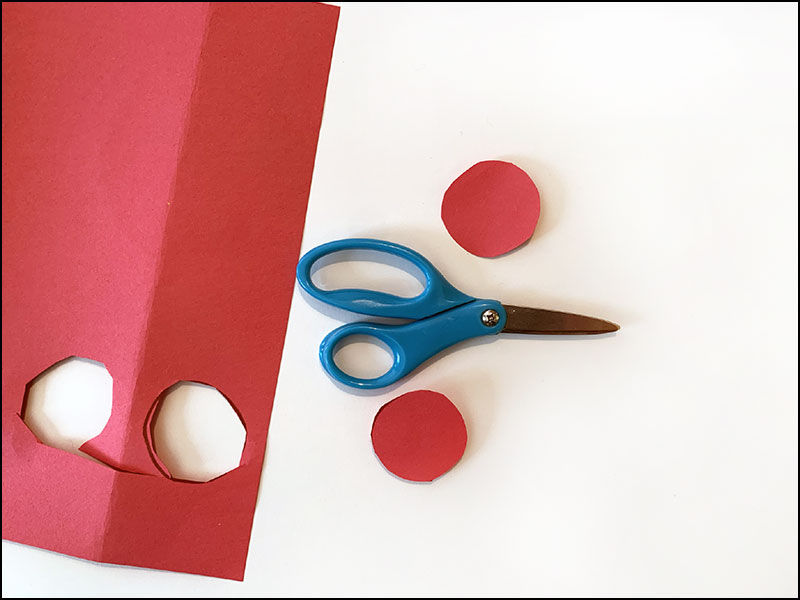 scissors next to red construction paper with two red circles cut