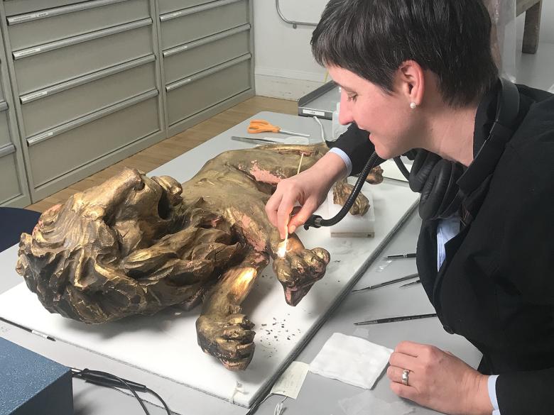 Conservator consolidating gilding on a sculpture of a lion