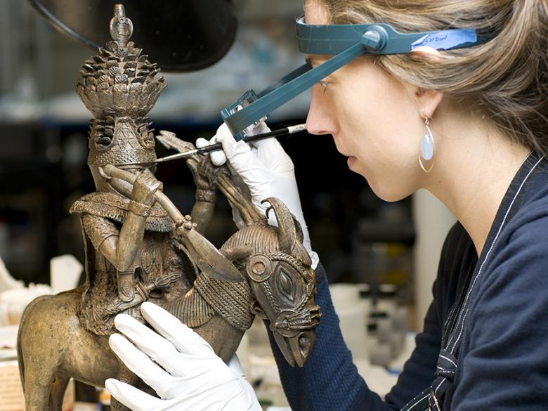 Conservator toning the surface of a copper alloy figure