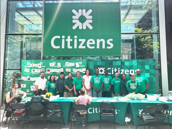 Staff from Citizens tabling at open house event, gathered underneath large Citizens banner