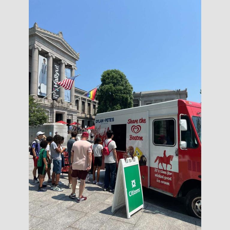 Citizens logo on sandwich sign in front of ice cream truck distributing treats to line of visitors outside Museum's Huntington Avenue Entrance