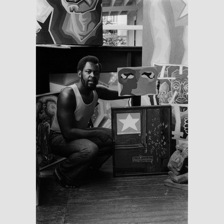 Black and white photo of a man kneeling in front of a number of painted canvases.