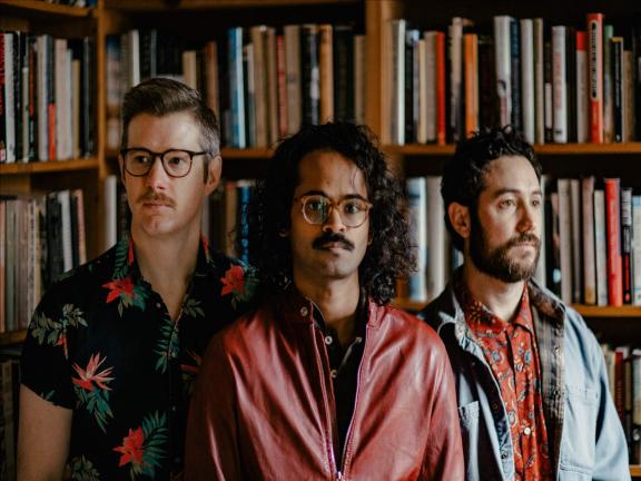Members of Darlingside standing in front of wall of bookcase