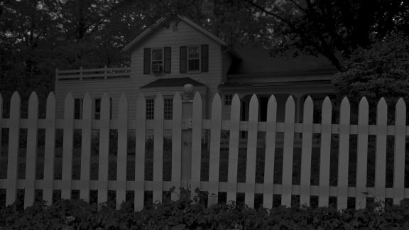 white picket fence with front of white-sided house visible in background; dark tones throughout