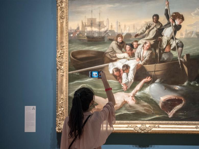 Young visitor holding up smartphone to take photograph of Copley's Watson and the Shark painting