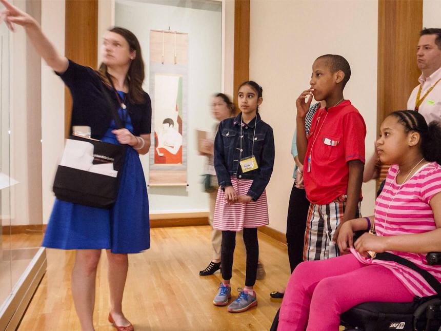 Museum guide pointing into a case while group of young visitors look on