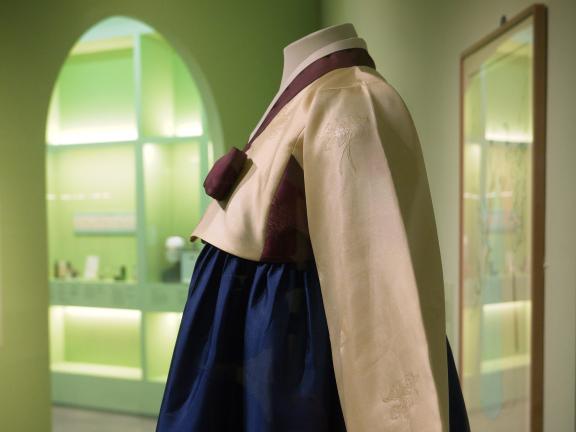 A hanbok seen from the side and waist up in a brightly lit green gallery.