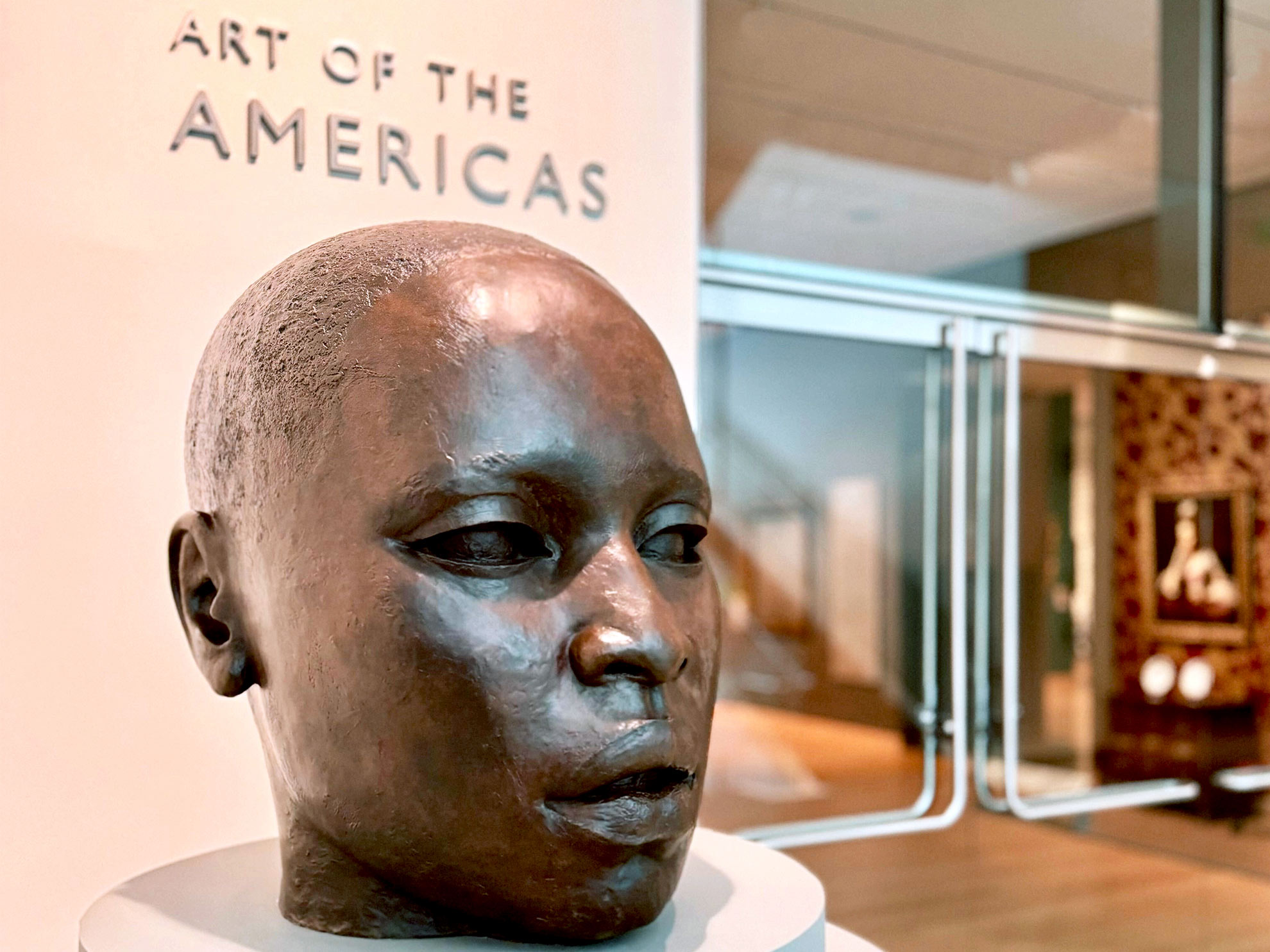 A large bronze sculpture of a head displayed at the entrance to the Art of the Americas wing