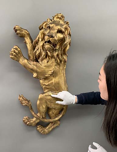 Conservator holding paper fill in place while the Lion Rampant is hanging on the wall