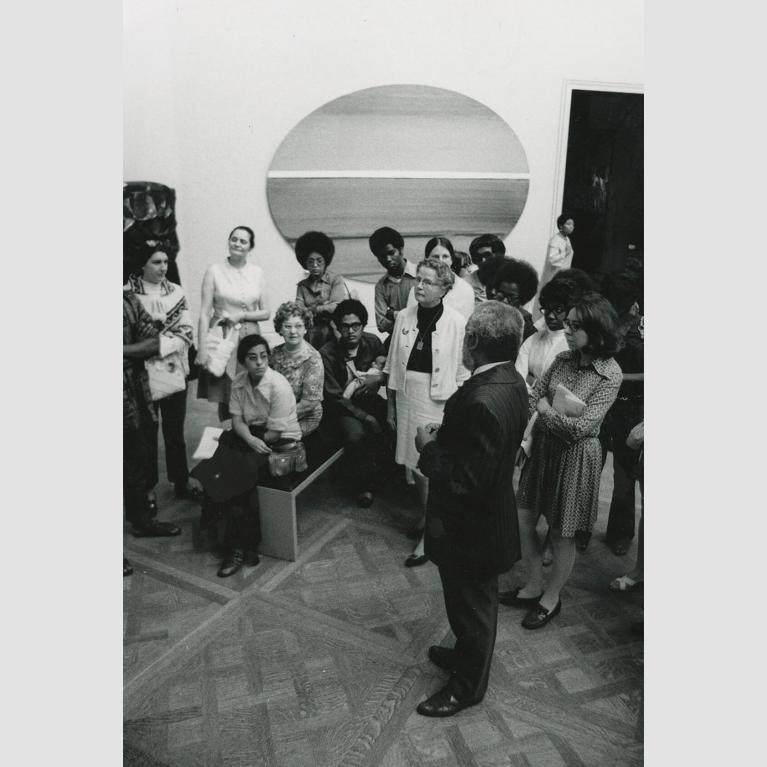 A crowd of people gathers around a man in an art gallery.