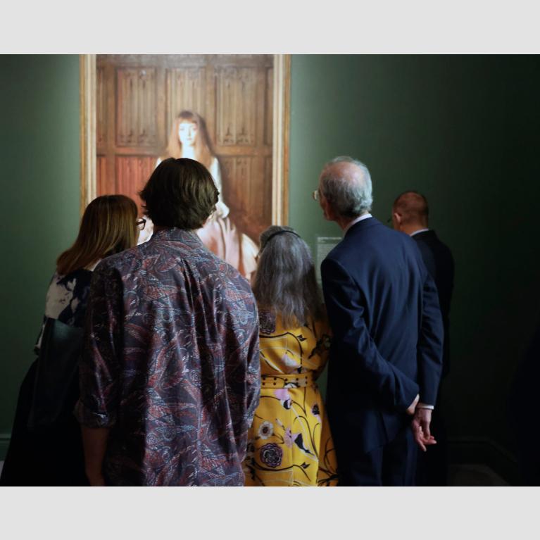 Visitors in "Fashioned by Sargent" exhibition, gathered closely around portrait of a young girl in a dress
