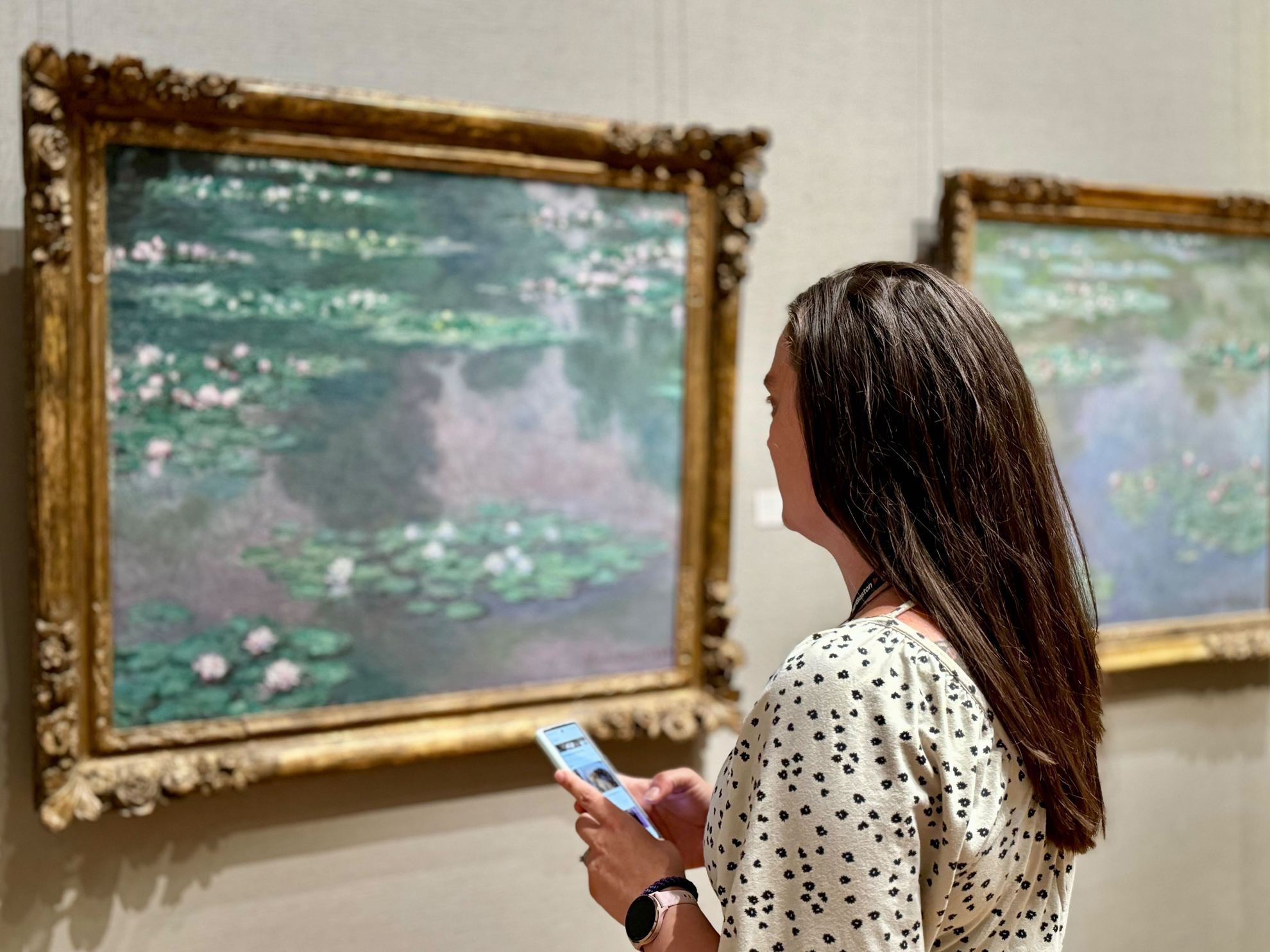 A visitor looks at a painting by Monet and engages with her smartphone