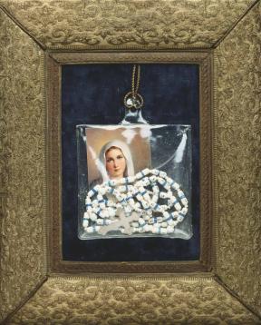 A picture of the Virgin Mary and a rosary hanging in a plastic bag against a dark blue background within a gold frame.