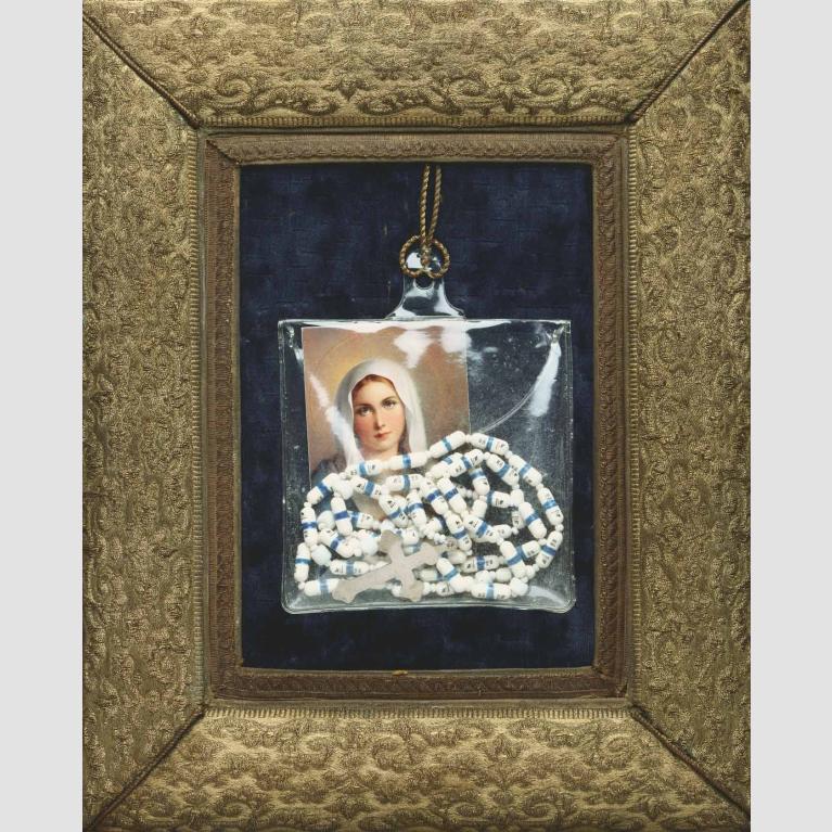 A picture of the Virgin Mary and a rosary hanging in a plastic bag against a dark blue background within a gold frame.