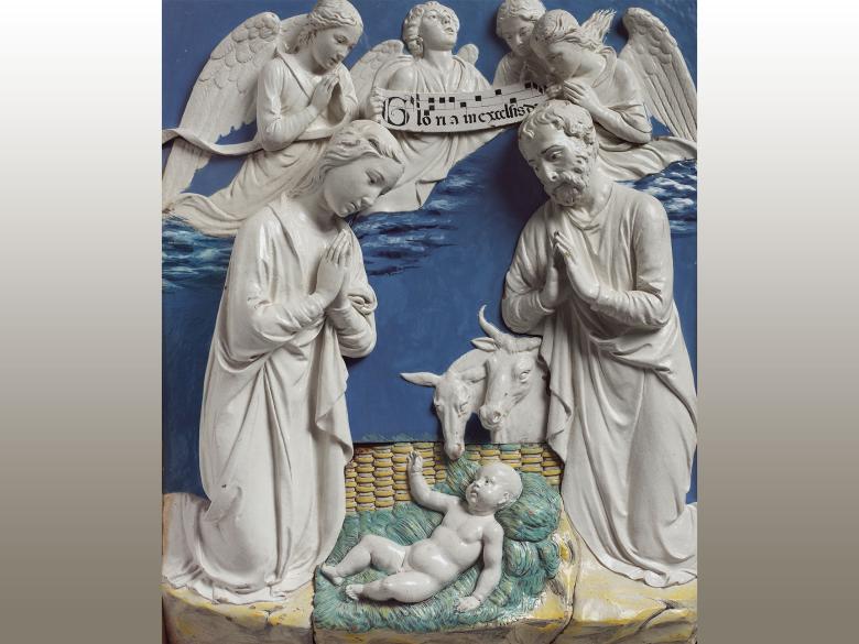 A relief of the Nativity scene: Mary, Joseph, and two farm animals look down upon a baby Jesus as four angels hover in sky holding a sign that reads "Gloria in excelsis deo"