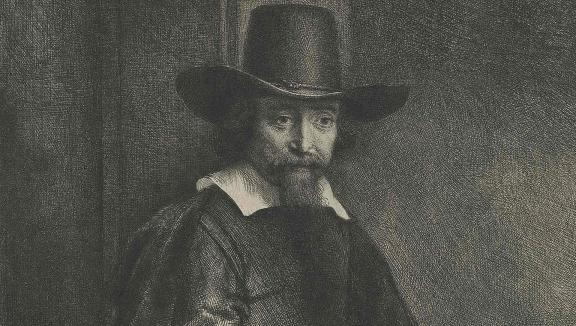 A bearded man wears a black hat and looks sternly at the viewer.