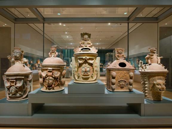 view of six Mayan urns arranged in a row inside a gallery case