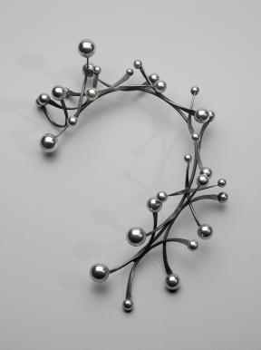 A photograph of a rigid, silver necklace decorated with thin metal pieces that have silver balls on each end.
