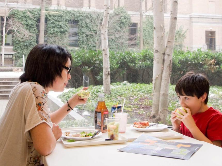 Parent and child eating lunch at table next to large window looking into outdoor courtyard