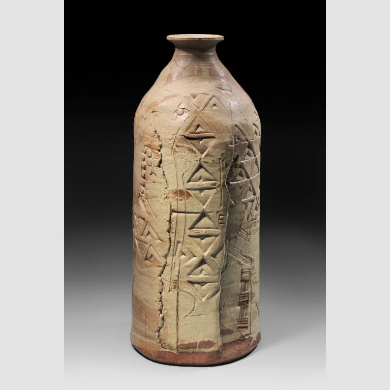 A light tan, cylindrical stone vessel with a tapered opening and varied carvings.