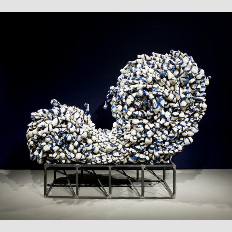 A group of amorphous blue-and-white ceramics are wired together in the shape of a cresting wave.