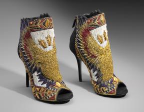 A pair of black suede heeled booties embroidered with a double-headed eagle in gold, red, and blue on the center front with wings extending upwards towards the back of the shoes. 