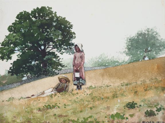 A boy lies in a field while a girl stands next to him.