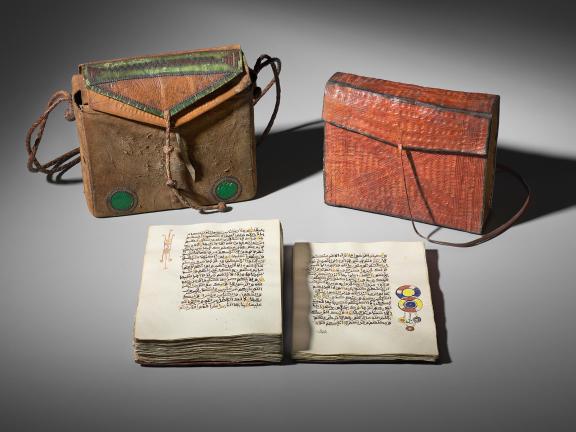 A qur'an open in front of two ornamented leather satchels.