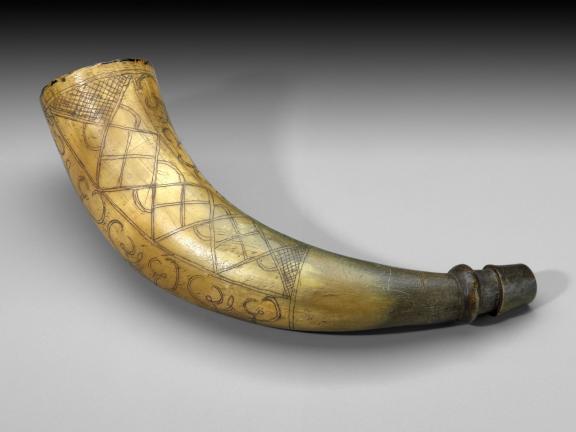 photo of a cow horn with carved geometric designs and worn, brown tip