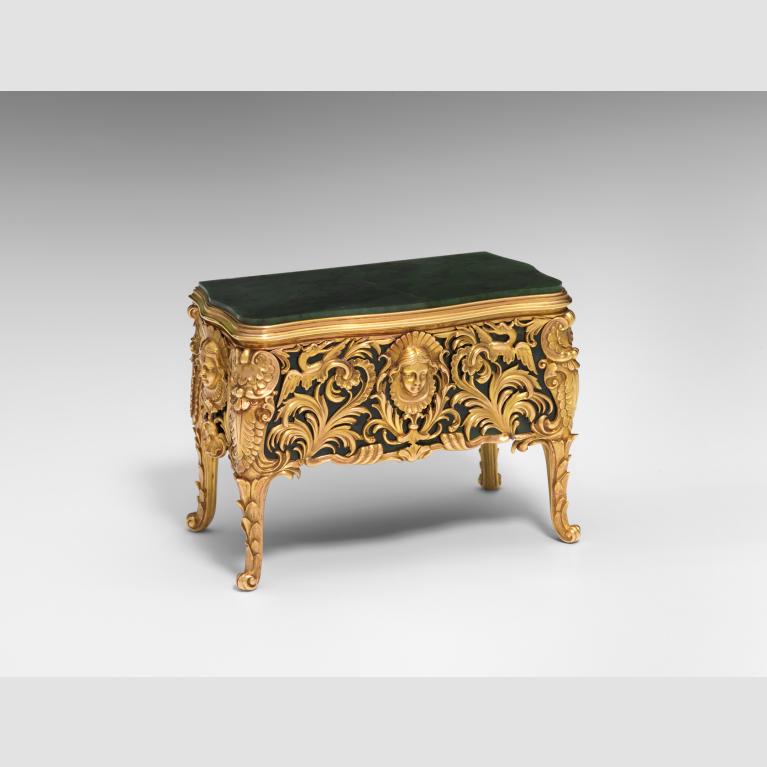 A green miniature commode with gold legs and adorned with intricate gold work.
