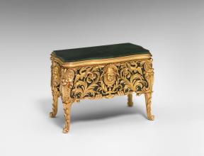 A green miniature commode with gold legs and adorned with intricate gold work.