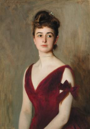 A woman sits for a portrait in a burgundy silk dress. 