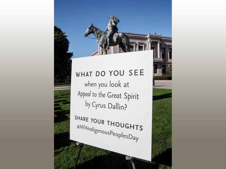 A sculpture of a Native American man on horseback stands on a pedestal. Signs surround the sculpture with visitor thoughts on the work of art.